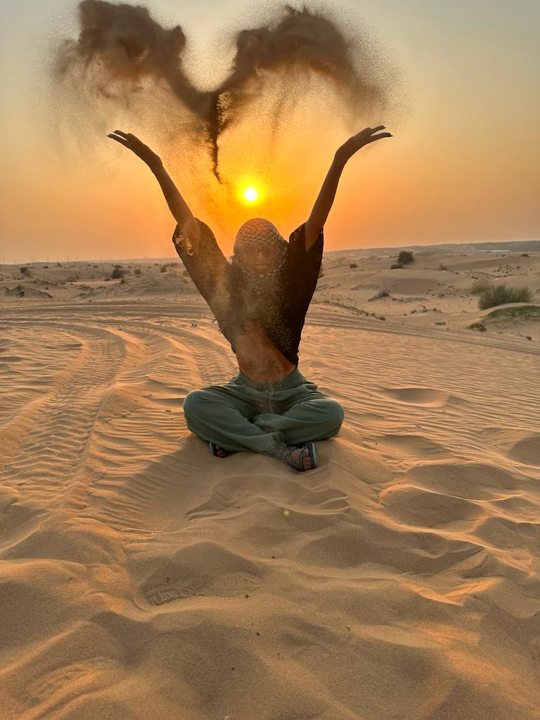 A woman standing in the desert with her hands raised in the air.